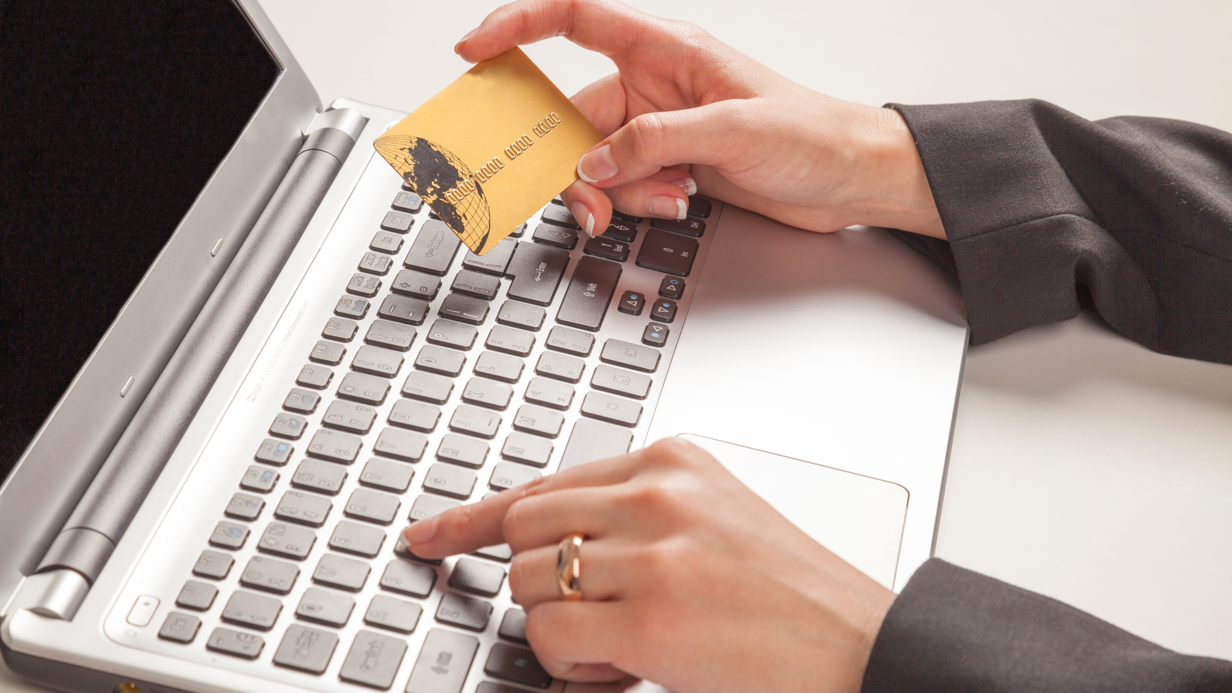 Woman holding gold credit card typing on laptop. Portrays as spending money online.