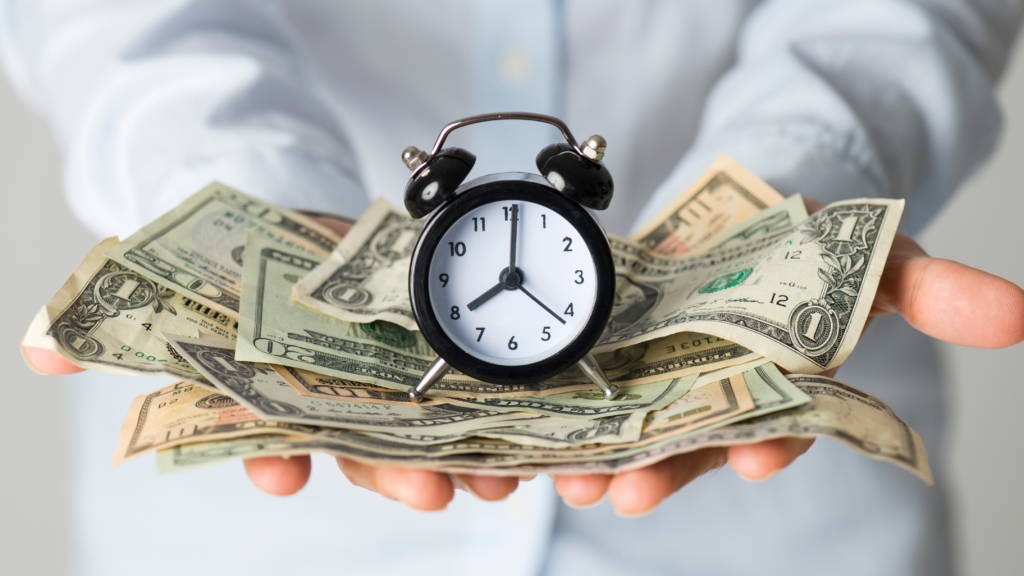 Hands holding a pile of cash with a alarm clock on top indicating time and cost savings